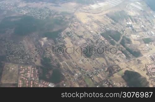 Earth landscape view from an airplane. Earth surface under the white clouds and blue sky from aerial view. Cloudy weather covering residential and argriculture land.