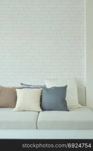 Earth tone color pillows on sofa with white brick wall in background