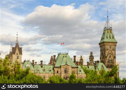 East Block building of the Parliament Hill in Ottawa, Canada. Beautiful view of the tops of East Block, emerging above the trees with white clouds sky in the background