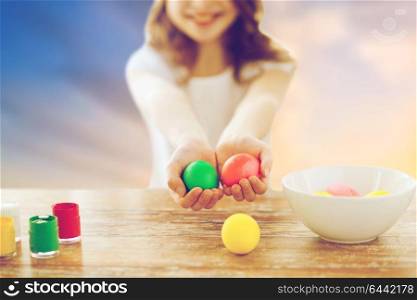 easter and holiday tradition concept - close up of happy girl holding colored eggs over sky background. close up of girl holding colored easter eggs