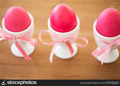 easter and holidays concept - pink colored eggs in ceramic cup holders with ribbon on table. pink colored easter eggs in holders on table