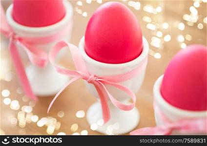 easter and holidays concept - pink colored eggs in ceramic cup holders with ribbon on table. pink colored easter eggs in holders on table