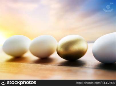 easter and object concept - close up of golden and white eggs on wood over sky background. close up of golden and white easter eggs on wood