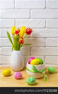 Easter arrangement with pink, green, yellow hand decorated eggs, red and yellow tulips in the white vase