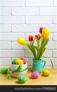 Easter arrangement with red, yellow tulips in the mint green pitcher and decorated eggs near painted brick wall