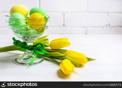 Easter background with green and yellow painted eggs in the glass vase and tulips. Happy Easter greeting card, copy space.