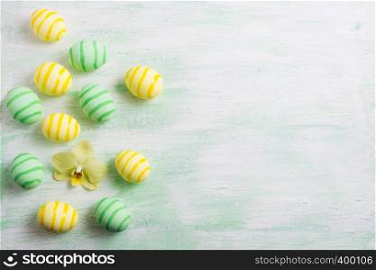 Easter background with green striped painted eggs and yellow orchid. Happy Easter greeting card, copy space.