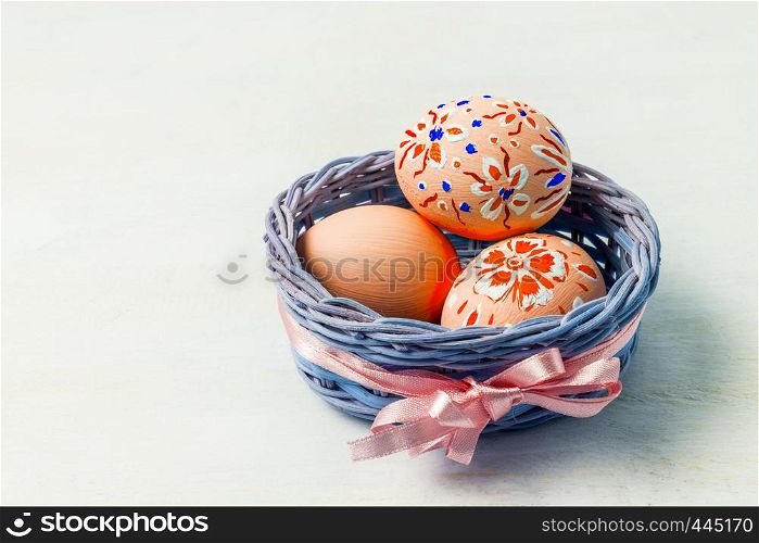 Easter background with painted eggs in the small blue wicker basket with pink silk ribbon. Happy Easter greeting card, copy space.