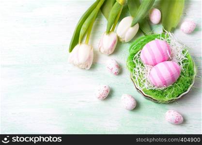 Easter background with pink striped painted eggs in the nest and white tulips. Happy Easter greeting card, copy space.