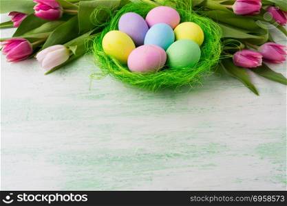 Easter background with purple, blue, pink, green, yellow painted eggs in green nest and tulips. Happy Easter greeting card, copy space.. Easter eggs in green nest background