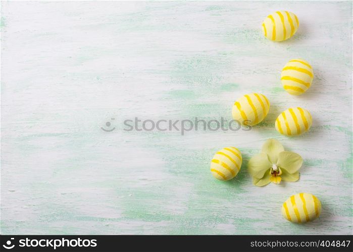 Easter background with yellow striped painted eggs and orchid. Happy Easter greeting card, copy space.