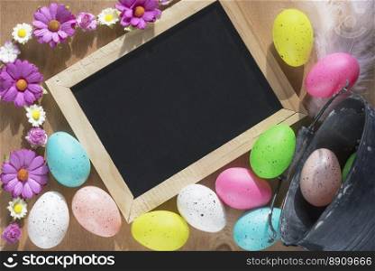 Easter banner with a rustic bucket full of painted eggs overturned on a table and a blank blackboard surrounded by spring flowers.