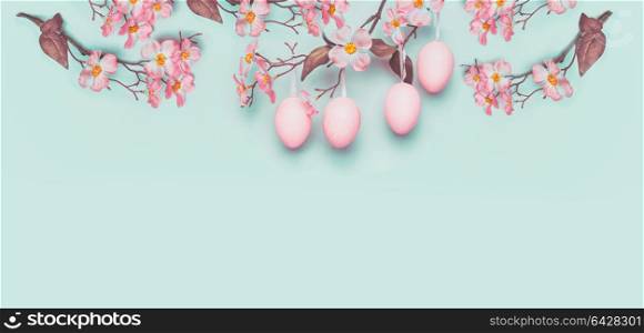 Easter banner with hanging pastel pink Easter eggs and spring blossom at light at blue turquoise background. Copy space