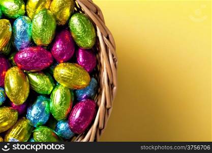 Easter basket with chocolate eggs on yellow paper background, Top view. Macro shot