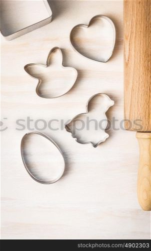 Easter biscuit cutter: rabbit, chicken, egg, heart and dough roll on white wooden background, top view, place for text