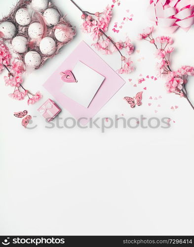 Easter blank greeting card mock up with pastel pink spring blossom flowers, eggs and hearts on white background, top view. Copy space for your design.