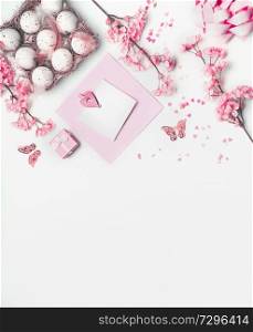 Easter blank greeting card mock up with pastel pink spring blossom flowers, eggs and hearts on white background, top view. Copy space for your design.