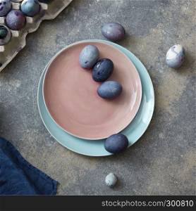Easter blue eggs on a ceramic plate in a color of Living Coral Pantone on a gray marble background with textile towel, place for text. Flat lay. Easter spring concept.. Glazed ceramic plate in a color of Living Coral Pantone with painted violet Easter eggs on a gray stone background, copy space. Top view.
