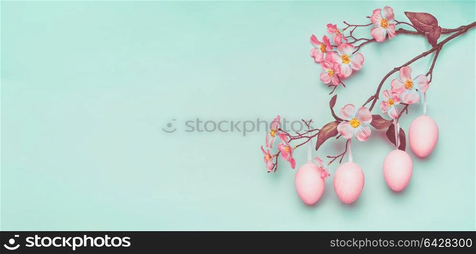 Easter border with hanging pastel pink Easter eggs and spring blossom at light at blue turquoise background.