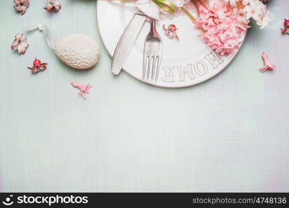 Easter border with table place setting with decor egg and flowers on light pastel wooden background, top view, place for text