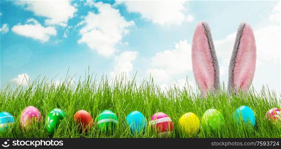 Easter bunny and Easter eggs on green grass meadow. Fun easter rabbit ears eggs and grass