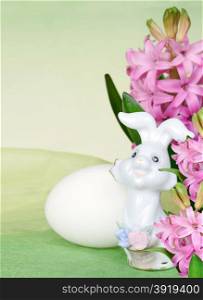 Easter bunny, pink flowers of hyacinth and white egg on a green background