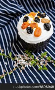 Easter cake, decorated with dried apricots and prunes, stands on a striped blue apron, a flowering branch. Easter religious holiday concept. Easter cake, decorated with dried apricots and prunes, stands on a striped blue apron, a flowering branch. Easter religious holiday concept.