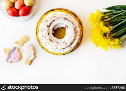 Easter cake, narcissus, cookies on white table background Happy easter backdrop for spring holiday. Top view. Copy space. Easter cake on white table background