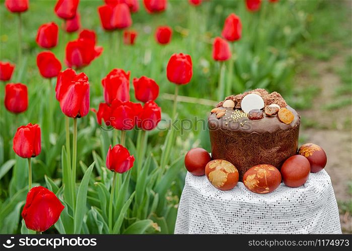 Easter cake on a background of red tulips in the garden. Festive composition on a blurry background of flowers on a clear sunny day.. Easter cake on a background of red tulips in the garden.