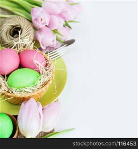 Easter composition: bouquet of pink tulips flowers and Easter eggs, plate and cutlery, with copy-space