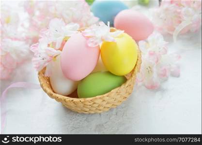 Easter composition with multicolored easter eggs in a wicker basket on the background of delicate pink flowers of the cherry blossoms