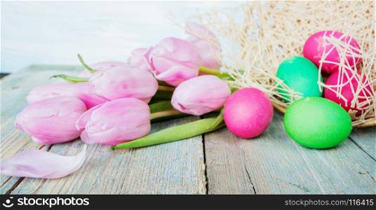 Easter composition with pink tulip flowers, painted Easter eggs and wicker basket are on the old blue wooden background