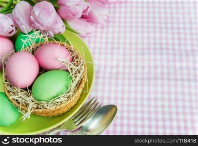 Easter concert: bouquet of pink tulips flowers and Easter eggs, plate and cutlery on checkered tablecloth, with copy-space