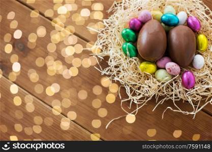 easter, confectionery and holidays concept - chocolate eggs and candies in straw nest on wooden background. chocolate eggs and candies in straw nest