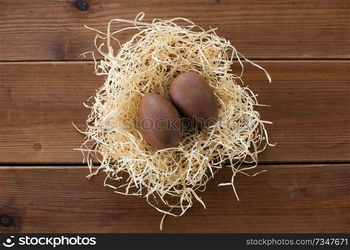 easter, confectionery and holidays concept - chocolate eggs in straw nest on wooden background. chocolate eggs in straw nest on wooden background