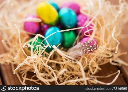 easter, confectionery and holidays concept - chocolate eggs in straw nest on wooden table. chocolate easter eggs in straw nest on table