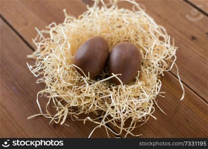 easter, confectionery and holidays concept - chocolate eggs in straw nest on wooden table. chocolate eggs in straw nest on wooden table