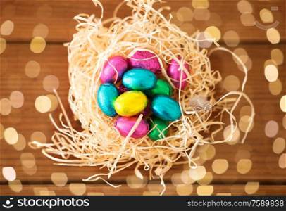 easter, confectionery and holidays concept - chocolate eggs in straw nest on wooden table. chocolate easter eggs in straw nest on table