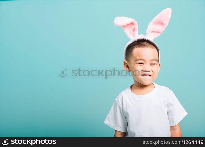 Easter day concept, Happy Asian cute little child boy smile beaming wearing bunny ears and white T-shirt standing on blue background with copy space
