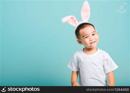 Easter day concept, Happy Asian cute little child boy smile beaming wearing bunny ears and white T-shirt standing on blue background with copy space