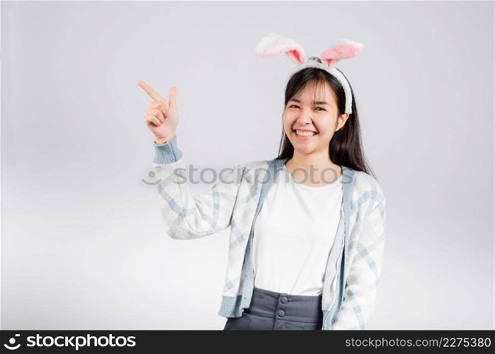 Easter day concept. Smiling happy woman wearing rabbit ears pointing finger something out space away side, studio shot isolated on white background with copy space