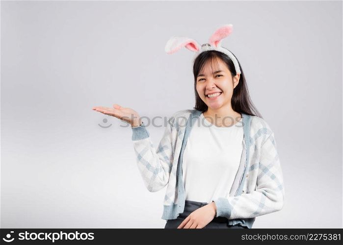 Easter day concept. Smiling happy woman wearing rabbit ears presenting product holding something on palm away side, studio shot isolated on white background with copy space