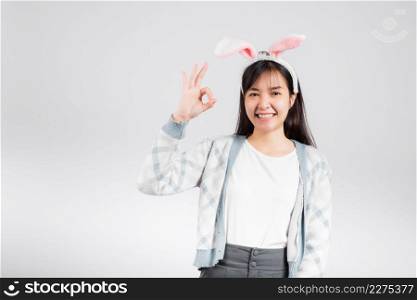 Easter day concept. Smiling happy woman wearing rabbit ears show OK finger sign, studio shot isolated on white background with copy space