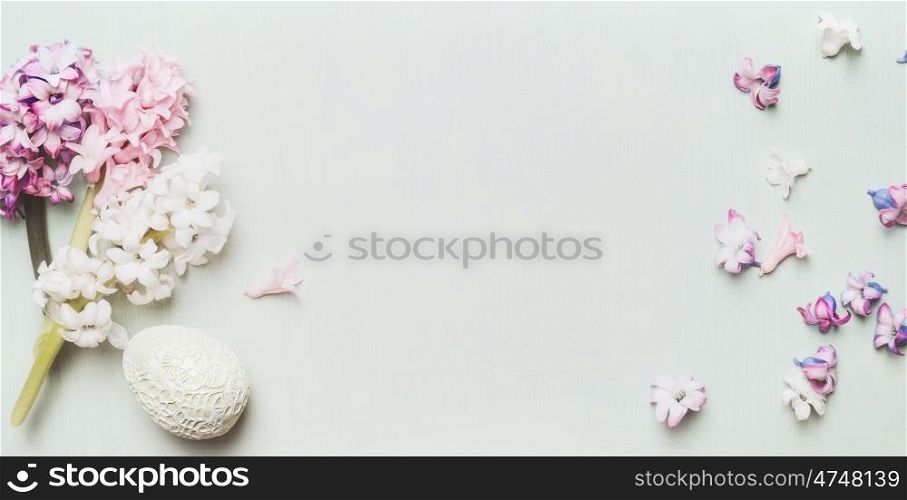 Easter decor egg with hyacinths and petal on light pastel wooden background, top view, place for text, banner