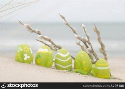 Easter decorated eggs and catkin on sand. Beach and ocean in the background