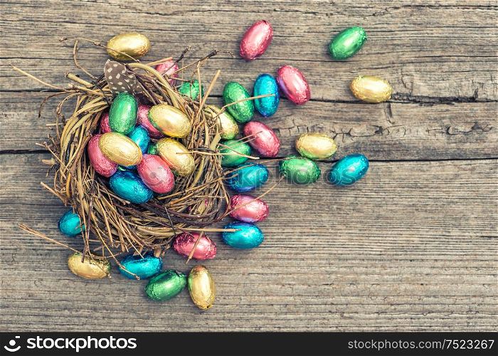 Easter decoration. Chocolate eggs in nest on wooden background. Vintage style toned picture