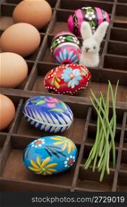 Easter decoration concept - brown chicken eggs, painted eggs with floral motif, green chive and woolen bunny in a vintage drawer (shadow box)