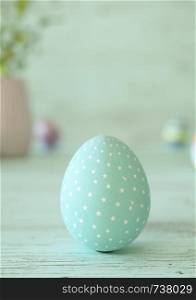 Easter egg standing on its blunt end, decorated in blue stars. Close-up view with blurred cyan background with copy space