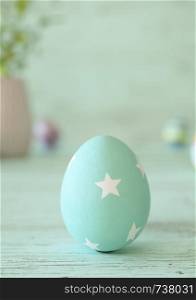 Easter egg standing on its blunt end, decorated in blue stars. Close-up view with blurred cyan background with copy space