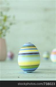 Easter egg standing on its blunt end, decorated in colorful stripes. Close-up view with blurred cyan background with copy space